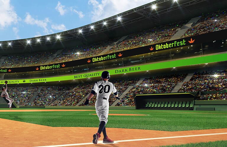 A baseball game is being played at a crowded baseball stadium. In the stadium, Ribbon Board LEDs are installed around the walls of each floor, and the screen is showing beer advertisements.