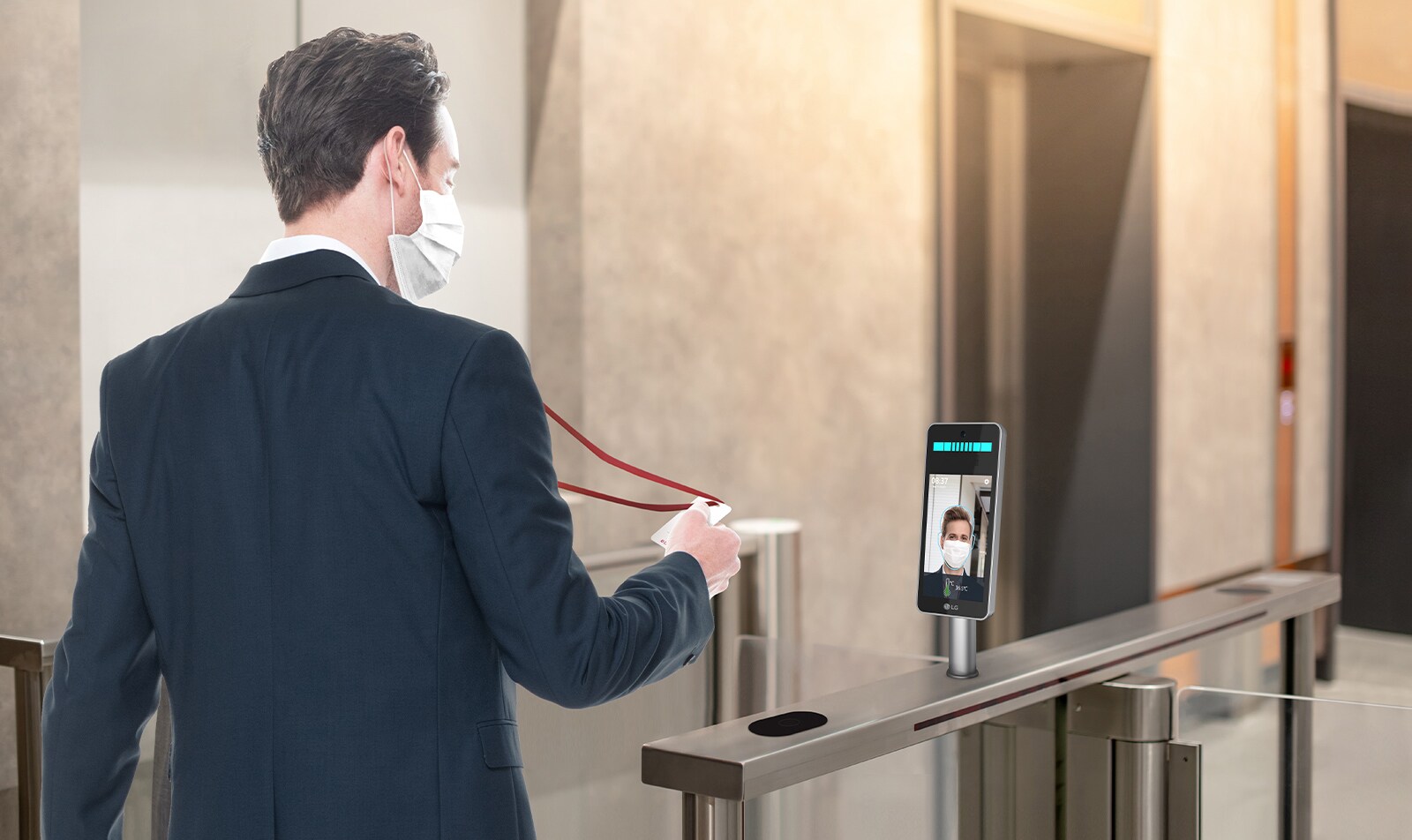 The employee with a mask clocks-in and enters the lobby of the company. LG Thermal Sensing Terminal is checking his fever.