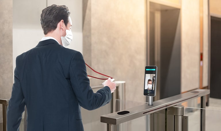 The employee with a mask clocks-in and enters the lobby of the company. LG Thermal Sensing Terminal is checking his fever.