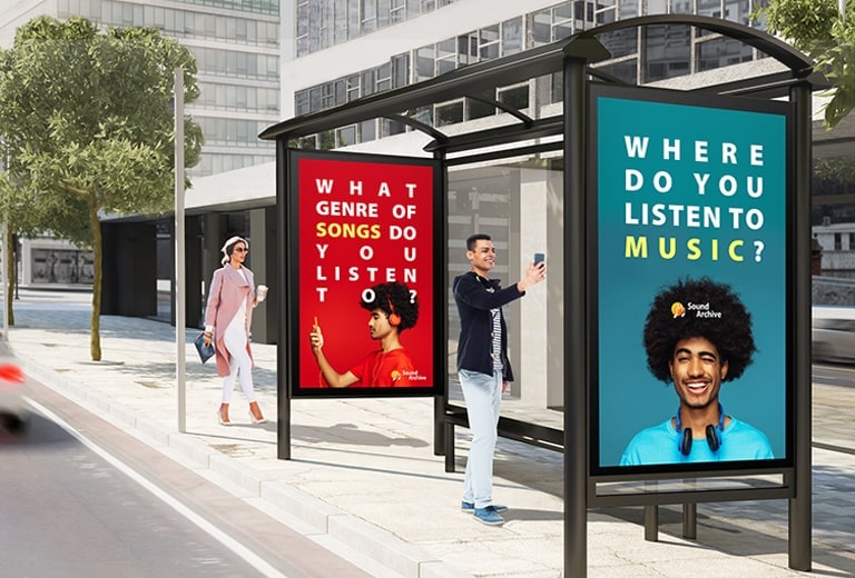 Large double-sided displays are installed at both ends of the bus station. Advertisements are being displayed on both sides of the displays, and people are watching advertisements inside and outside of the bus stop at the same time.