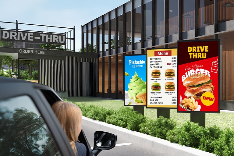 Outdoor displays are installed in the drive-thru zone of the burger place, vividly showing menus and images even in bright sunlight.