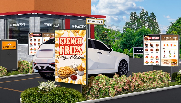 Several outdoor displays are installed at a burger place’s drive-thru, clearly and brightly showcasing the menu and food images.