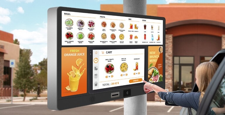22XF1TJ is installed as a touch kiosk for drive-in ordering. A woman is touching a kiosk to select a food from the menu.