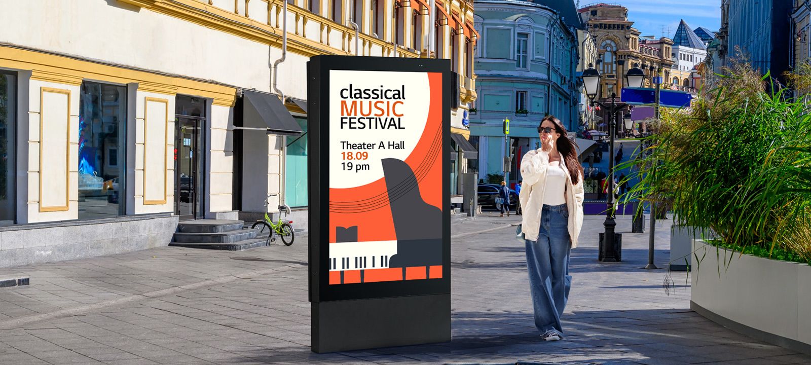 A large-sized display is installed on the street, and a woman is looking at a vivid-quality advertisement on the screen.