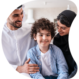 A smiling man with a beard is seated next to a woman in a headscarf, with a young boy smiling between them, depicting a happy family.