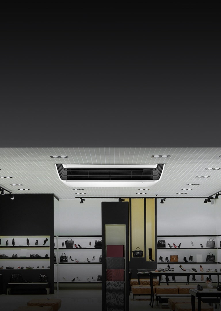 LG Ceiling Suspended air conditioning unit, with a white body and black front, mounted on a lighted ceiling.