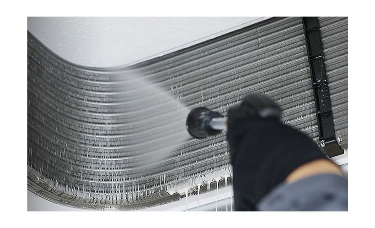 A man donning a safety helmet is diligently covering an open indoor unit perched on the ceiling with a protective plastic cover.