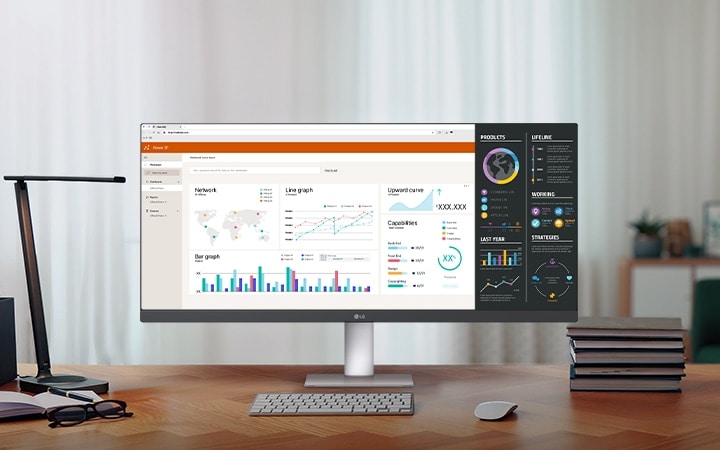 A modern home office setup featuring a large ultra-wide LG monitor displaying data dashboards and graphs, with a wireless keyboard and mouse on a wooden desk.	