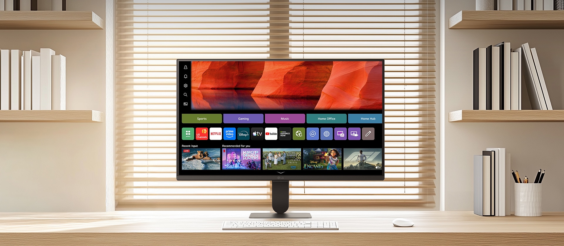 LG Smart Monitor on a clean wooden desk in a bright home office, displaying the webOS home screen with streaming apps and content tiles, paired with keyboard and mouse, bookshelf and window blinds in the background, highlighting smart entertainment and productivity use.