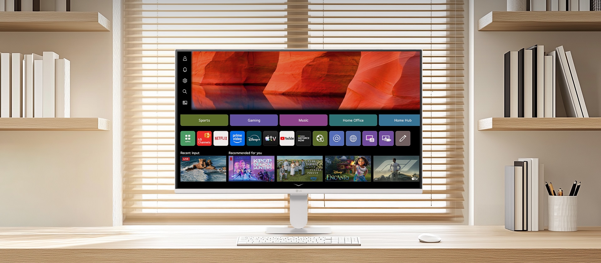 LG Smart Monitor on a clean wooden desk in a bright home office, displaying the webOS home screen with streaming apps and content tiles, paired with keyboard and mouse, bookshelf and window blinds in the background, highlighting smart entertainment and productivity use.