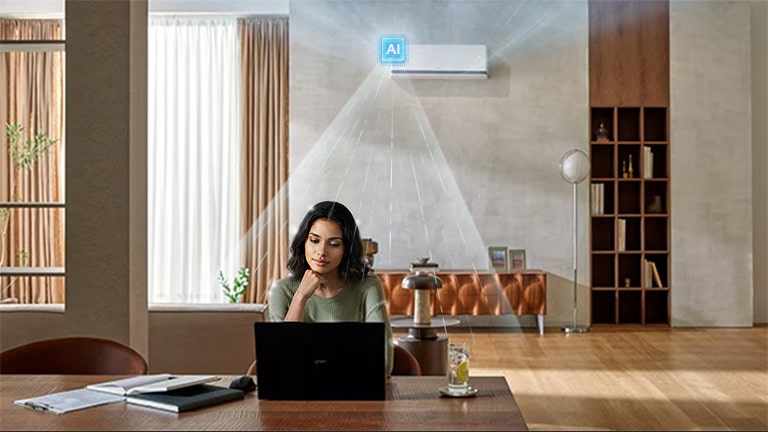 LG DUALCOOL AI air conditioner cooling a woman working at a desk with a laptop in a living room.