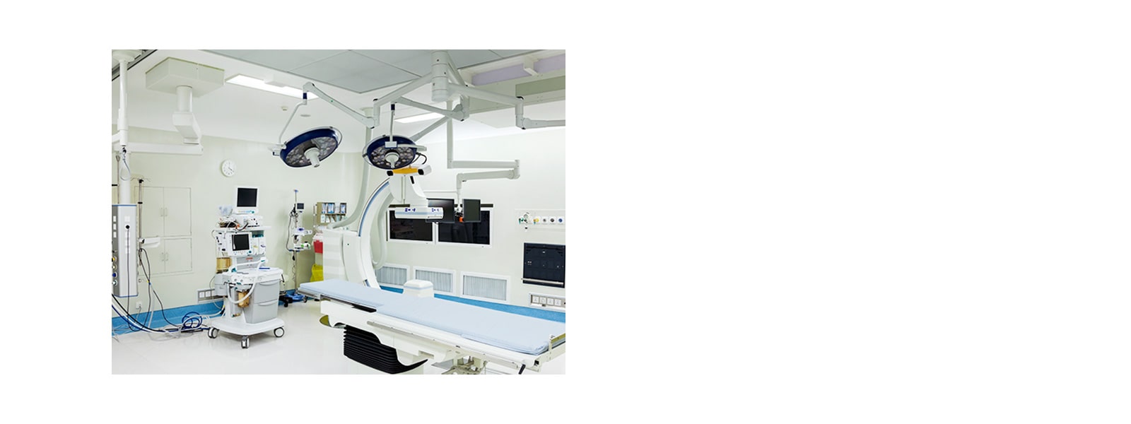 An operating room with white walls featuring patient's bed, multiple medical devices connected via electric cables and monitors with black screen.