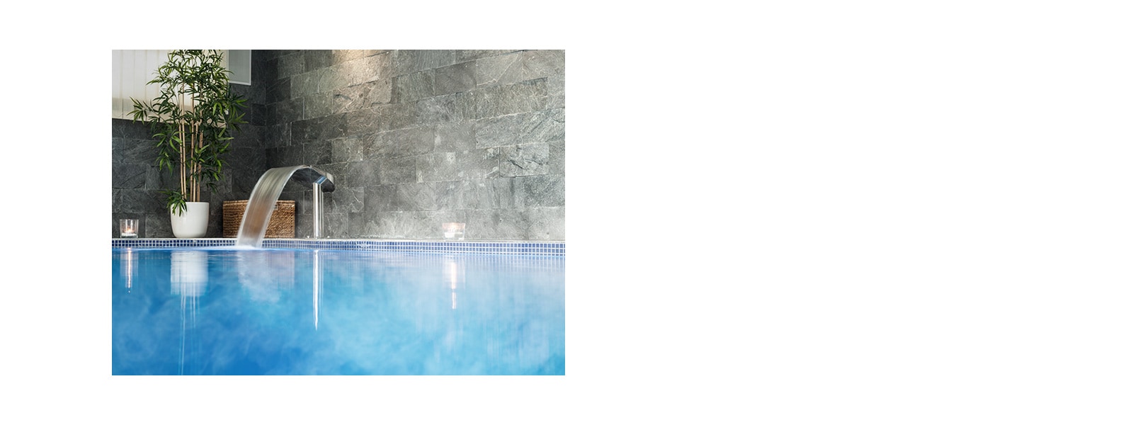 An indoor swimming pool with walls coverd with grey marble square tiles and an artificial waterfall to the left.