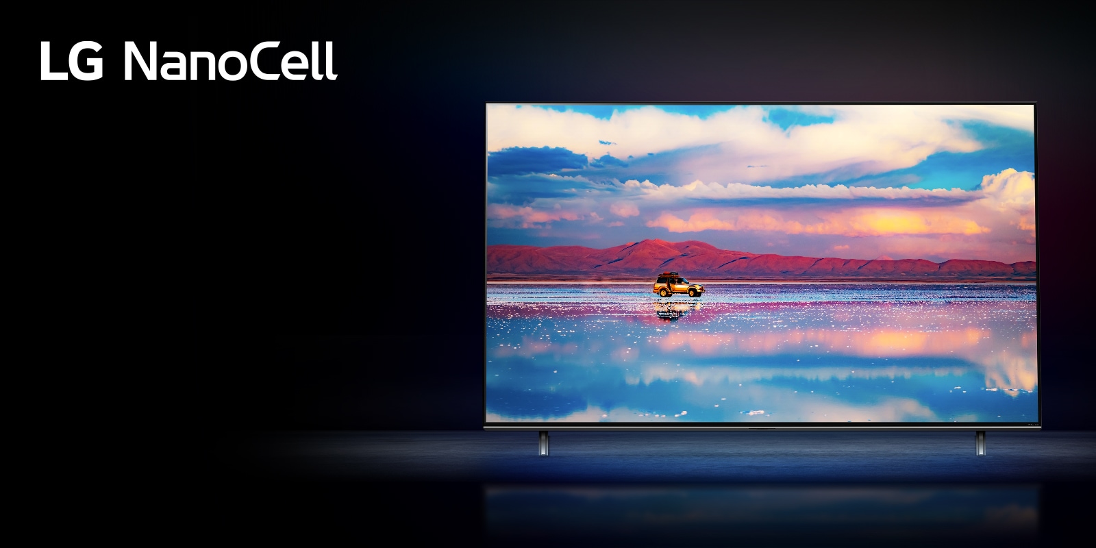 An LG NanoCell TV against a black background. The TV shows a car driving in front of a low mountain range in water that reflects the vivid sky.