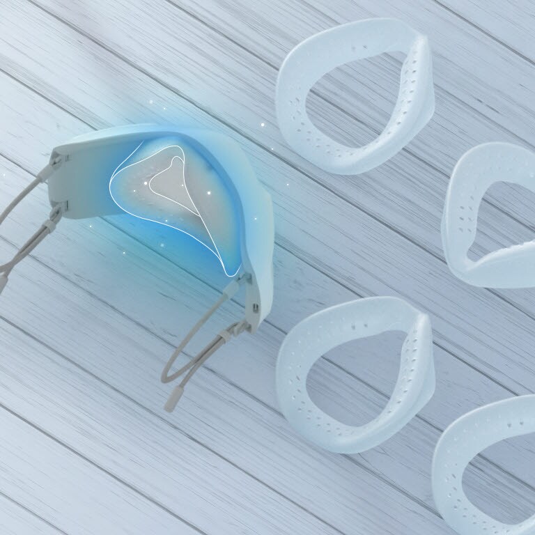 The top and slight interior of the mask is shown with the inner cover inside and silicone pads are spread on the table around it. The place to put the silicone pad inside is highlighted in blue.