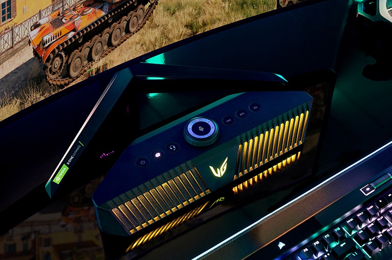 A top view of a gaming speaker with yellow lighting that fits under desktop and its v-shaped stand, there is a gameplay scene in bottom corner of a monitor