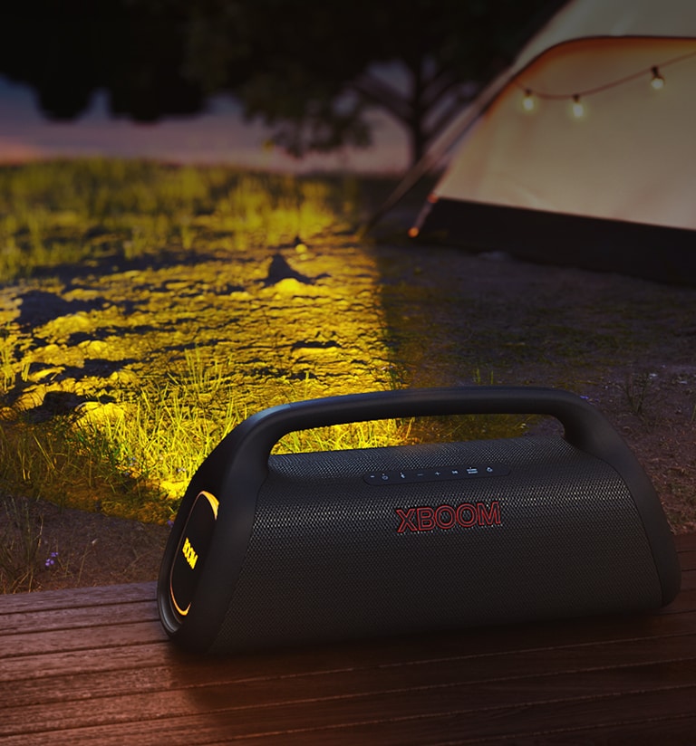 LG XBOOM Go is placed on the wooden deck. It casts a stage lighitng in the camp site.
