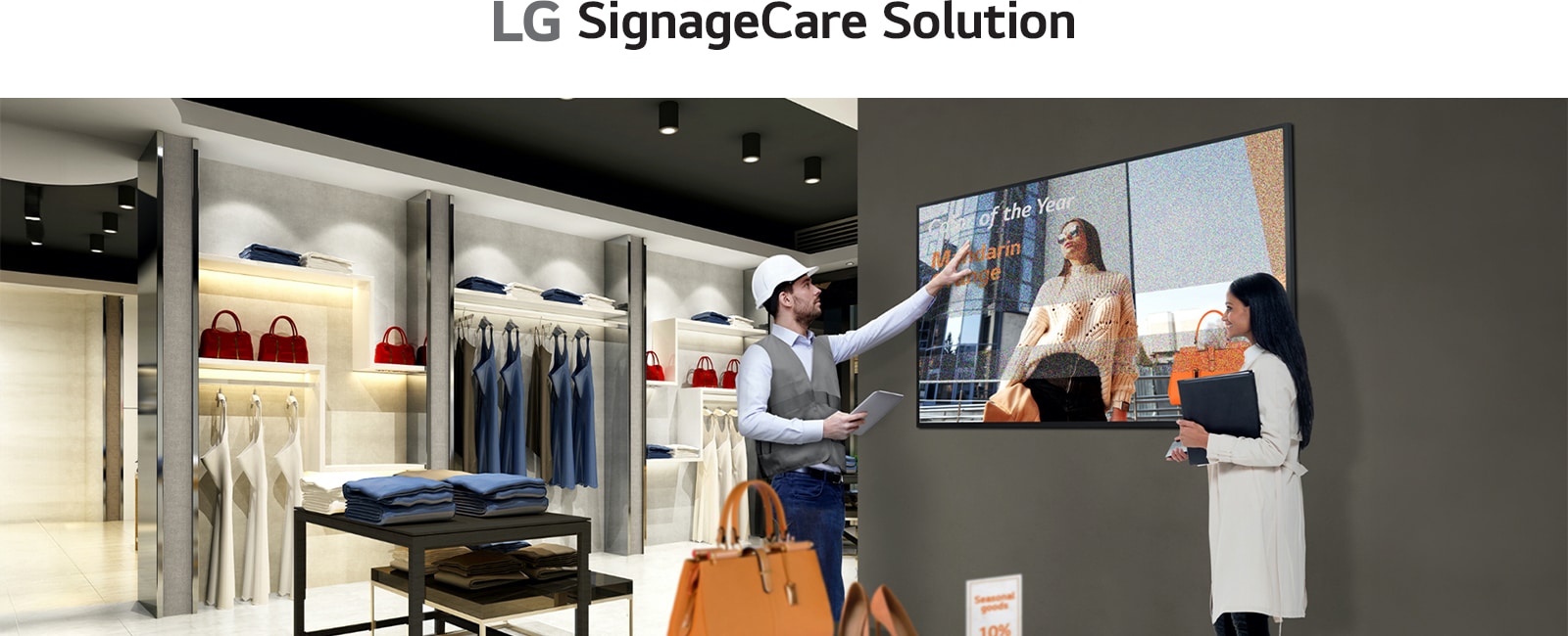 A retail store employee in a vest and hard hat gestures toward a digital display showing a woman with "Employee of the Year" text. Another person, holding a folder, observes the screen in a modern retail space with shelves of clothing and bags.