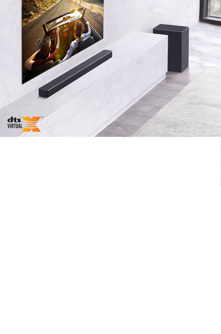 TV is on the wall, LG Soundbar is below on a white marble shelf with a sub-woofer to the right. TV shows a couple in a car. 