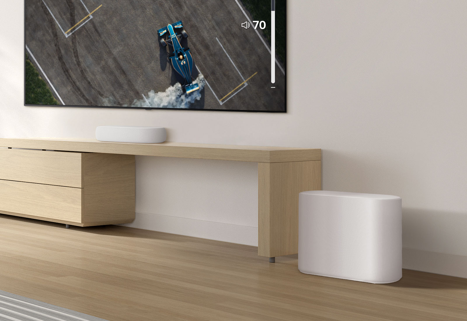 A soundbar is placed on a wooden table, a subwoofer is placed on a wooden floor. A mild sound wave effect comes out from the subwoofer on a floor. There is a TV placed above a soundbar. A racing car on a TV screen is driving very fast and violently and the GUI of TV volume is going up. 