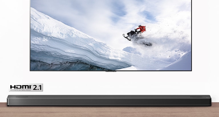 TV and Soundbar are seen from the front. TV shows man riding snowmobile in the snowy mountains. HDMI 2.1 logo is below TV. 