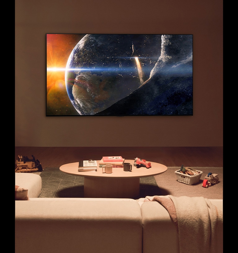 A family sat on the floor of a low-lit living room by a small table, looking up at an LG TV mounted on the wall showing the Earth from space.