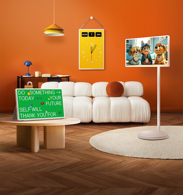 LG StanbyME 2 screens displayed in a modern living room. There is a StanbyME 2 on a stand, one is hung on the wall, and the other is propped up on a table using the folio cover.