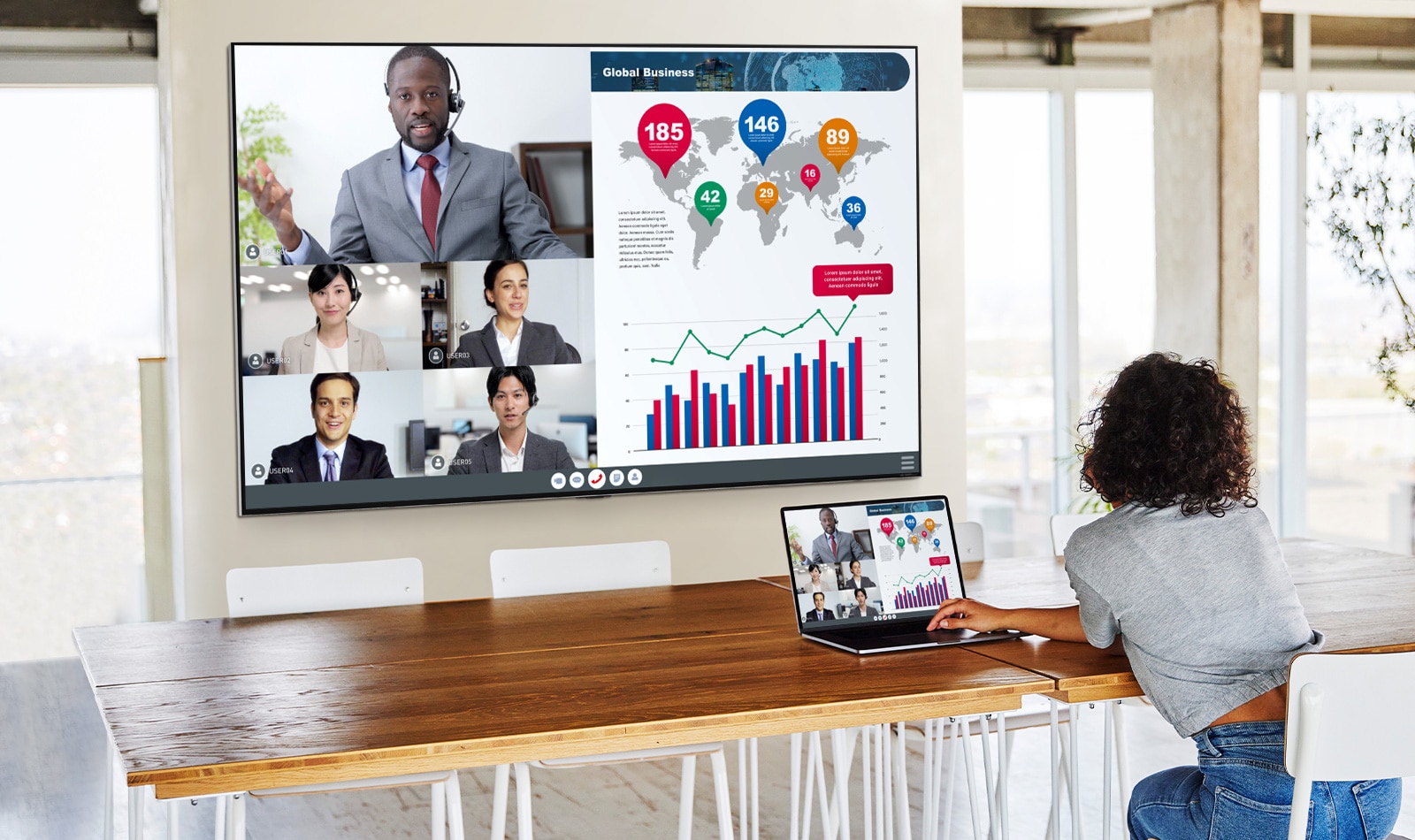 A woman is telecommuting with a laptop and a big tv hung on the wall in the living room.