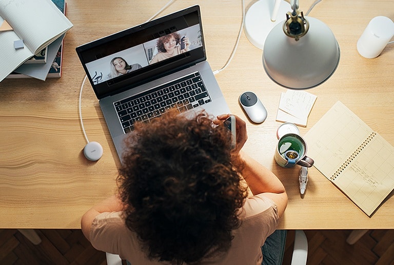 A woman is working on a computer and uses Plug and Wireless to participate in a conference call.