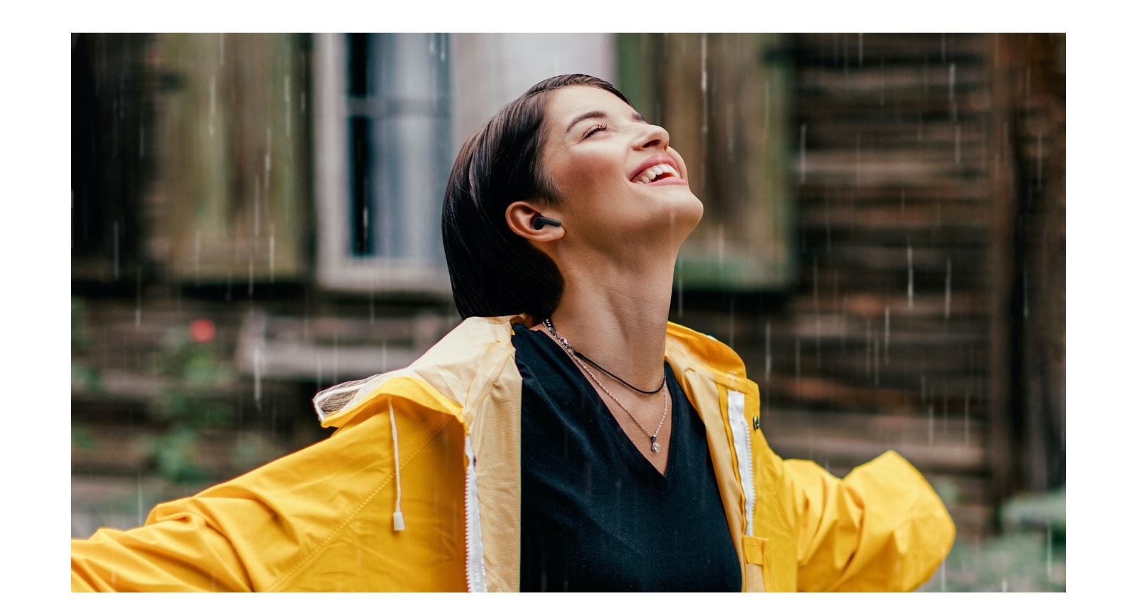 A woman wearing a bright raincoat listens to the earbuds while standing in the rain.