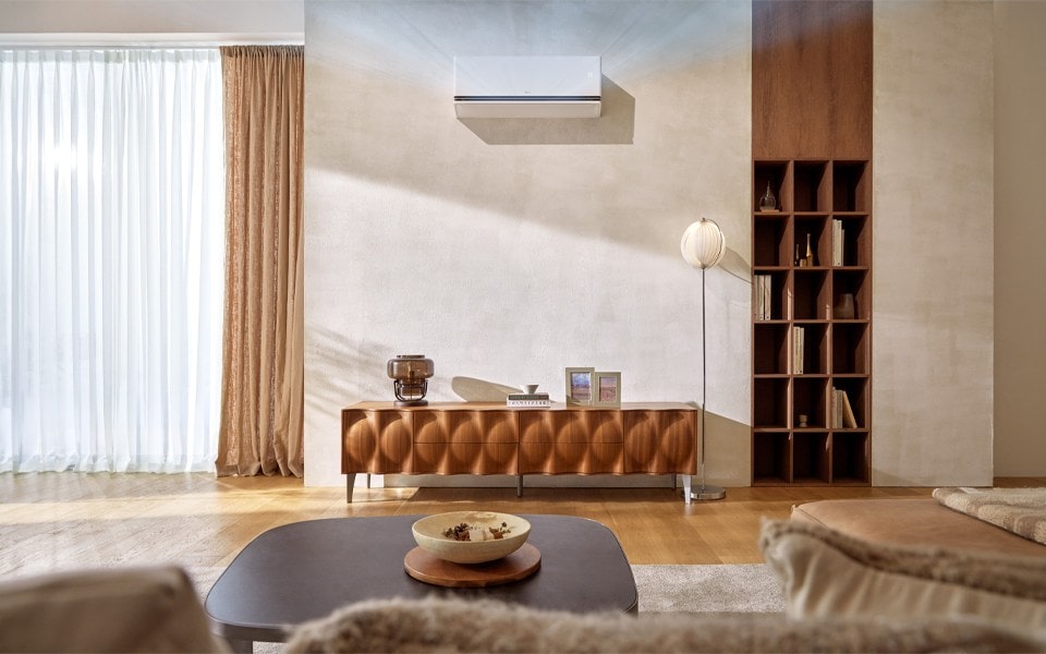 A wall-mounted LG air conditioner in a minimalist, sunlit living room with wooden furniture.