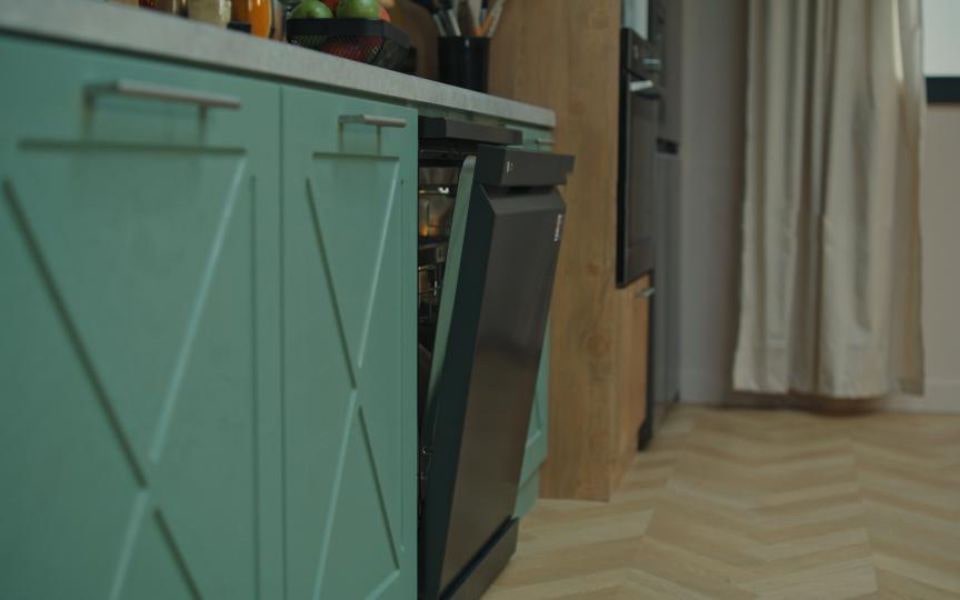 A black lg dishwasher slightly open in a modern kitchen with green cabinets.