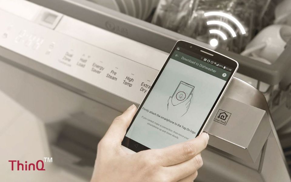Hand holding a smartphone near an LG dishwasher to connect to LG ThinQ via Wi-Fi.