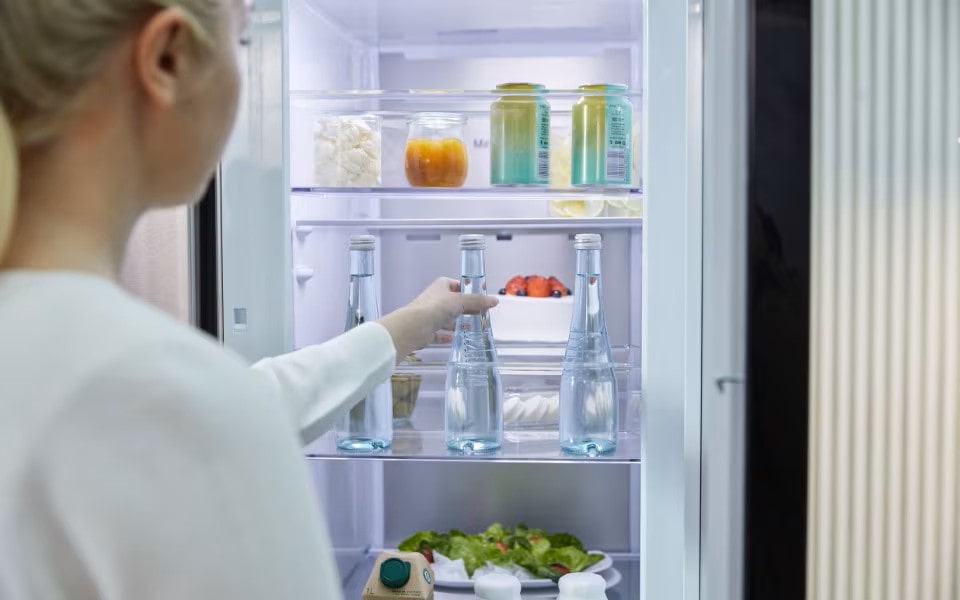A woman reaching for a bottle of water inside a brightly lit open LG refrigerator.