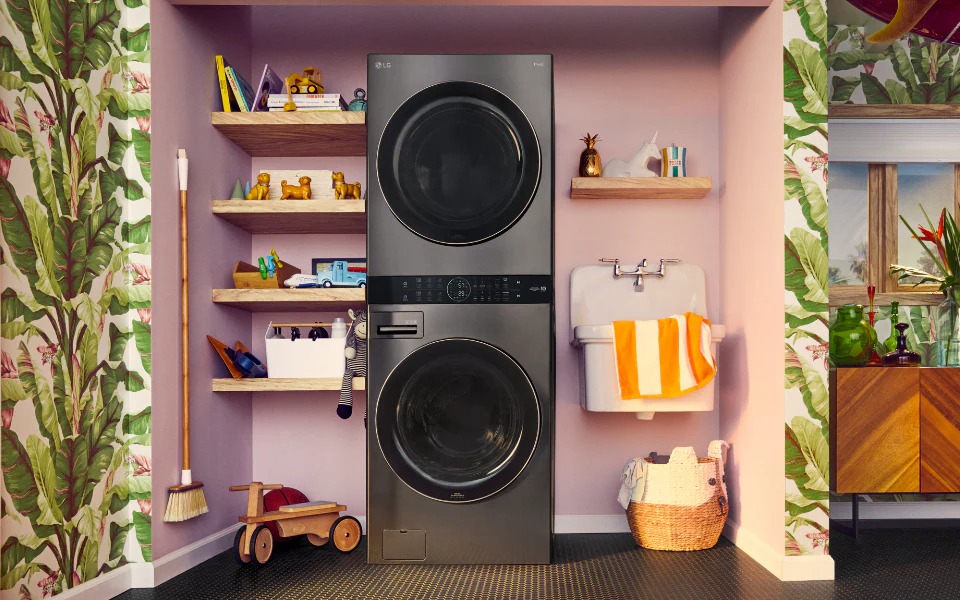 A stylish laundry room features a stacked LG washer and dryer, wooden shelves with decor, a small sink, and tropical wallpaper.