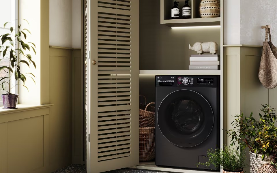 Dark LG washing machine in a modern laundry nook with louvered doors, shelving, and potted plants.