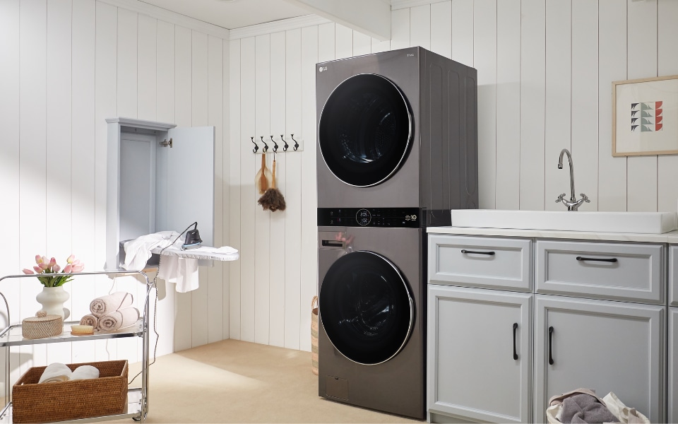 LG WashTower washer dryer in a bright laundry room with sink and storage cabinets.