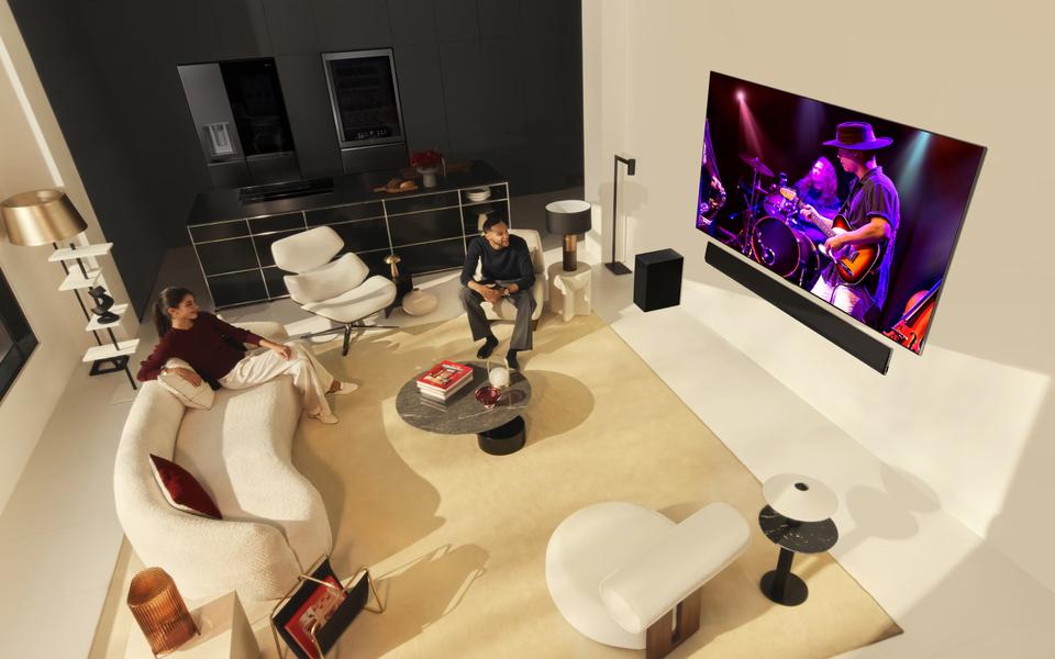 Modern living room with large TV showing a yellow sports car, man with dog on sofa, and ocean view through the windows.