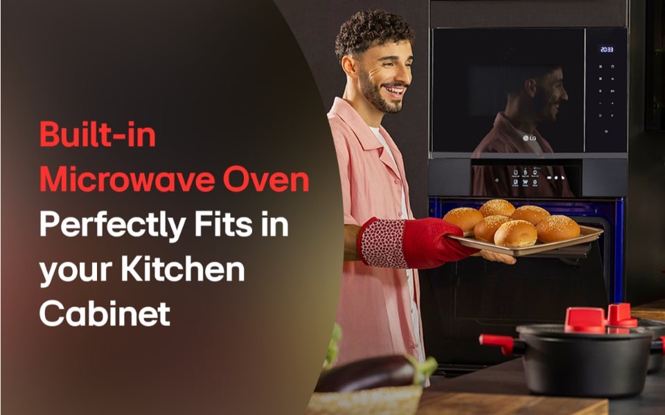 A man smiling while holding a tray of baked buns in front of a sleek LG built-in black microwave.