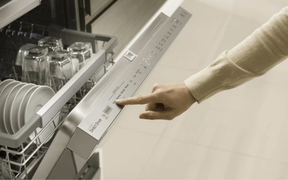 A woman selects a cycle on the top control panel of an open, loaded LG dishwasher