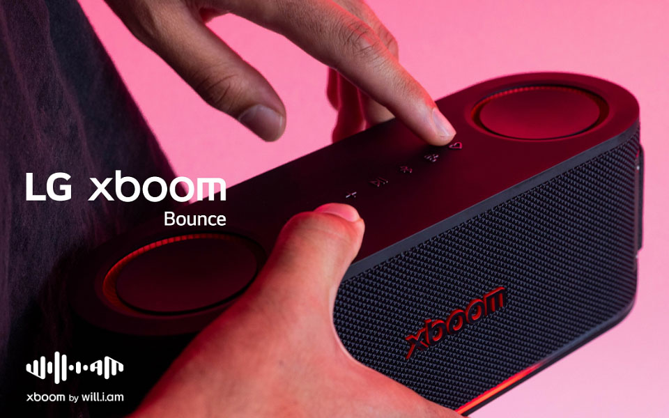 Close-up of a person holding an LG XBOOM Bounce speaker with pink lighting in the background.