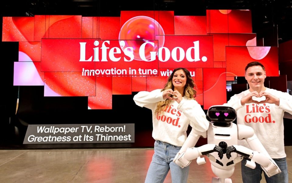 Two people and LG's CLOiD Robot pose with heart hand gestures in front of a LG 