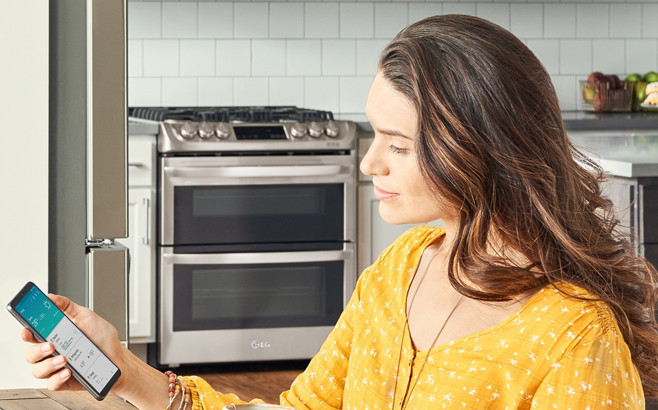 A woman looking at her smart phone shows LG ThinQ app on the smart phone screen