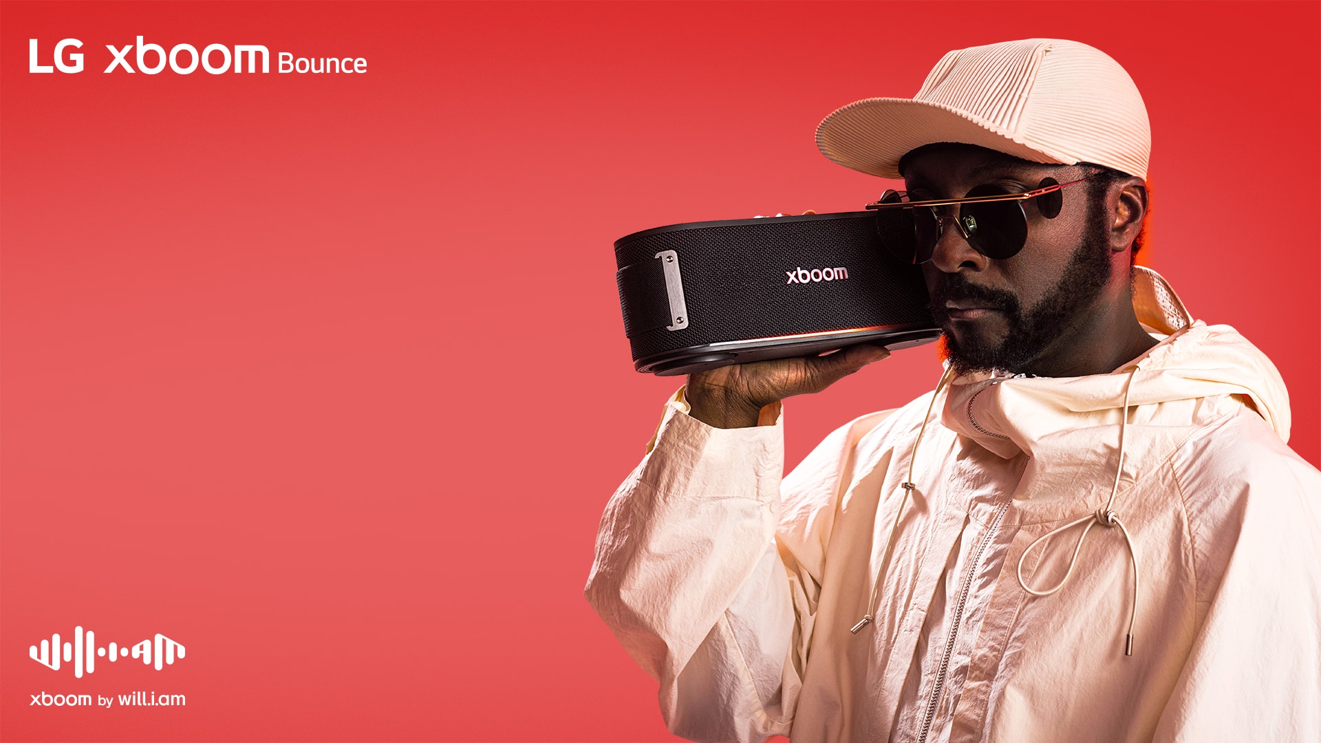 يظهر will.i.am مرتديًا زيًا أبيض ونظارات شمسية، وهو يحمل جهاز xboom Bounce قرب وجهه.
