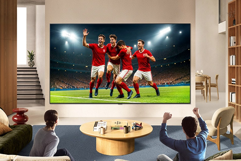 يُثبَّت تلفزيون LG TV لمشجعي الرياضة على الحائط في غرفة معيشة مشرقة، حيث يعرض لحظة احتفال في مباراة كرة قدم بألوان نابضة وجودة صورة مُحسّنة تمتد عبر شاشة واسعة، بينما تتشارك العائلة الجالسة على الأرائك أجواء الحماس والتشجيع.