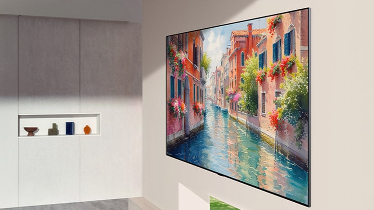يتميز تلفزيون LG OLED evo AI G6 بتصميم يشبه معرض الفنون، حيث يتم تركيبها بشكل متساوٍ مع سطح الحائط في مساحة معيشة عصرية، لتعرض مشهدًا نابضًا بالحياة لقناة مائية تزينها مبانٍ وأزهار ملونة، ينسجم بشكل طبيعي مع التصميم الداخلي الراقي.