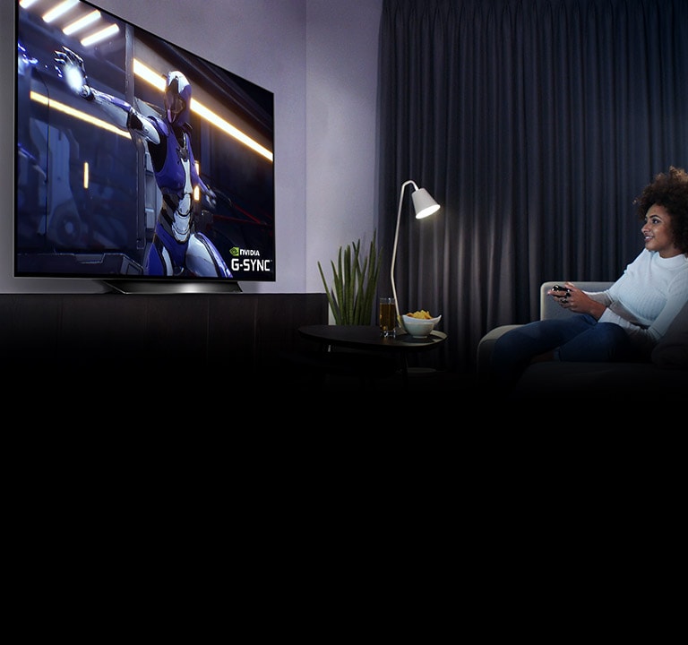 Woman sitting on a sofa, holding a joystick while playing a game on a TV screen