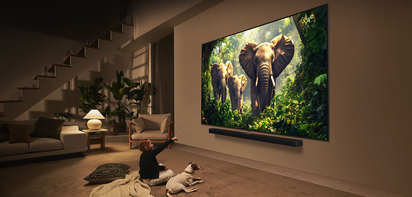 فتاة وكلب يجلسان أمام تلفزيون LG QNED TV مثبت على جدار يصور ثلاثة أفيال تسير للخارج فوق مكبر الصوت LG Soundbar. 
