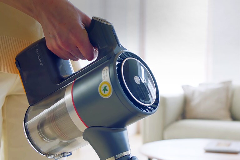 تظهر يد المرأة وهي تمسك مقبض المكنسة الكهربائية بكل أريحية أثناء تنظيفها لغرفة المعيشة.