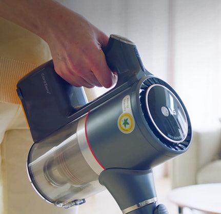 تظهر يد المرأة وهي تمسك مقبض المكنسة الكهربائية بكل أريحية أثناء تنظيفها لغرفة المعيشة.